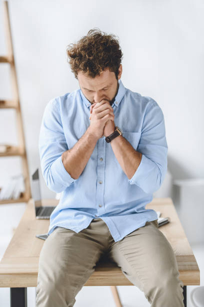 istock caucasian businessman praying while sitting on table in modern office 819674022
