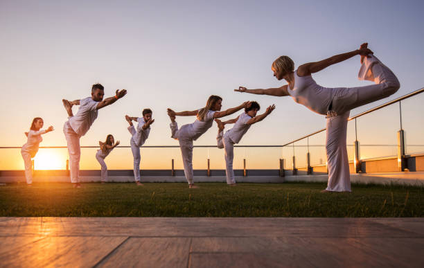 un grande gruppo di atleti che fanno esercizi di equilibrio yoga su un balcone al tramonto. - sunset yoga young men caucasian foto e immagini stock