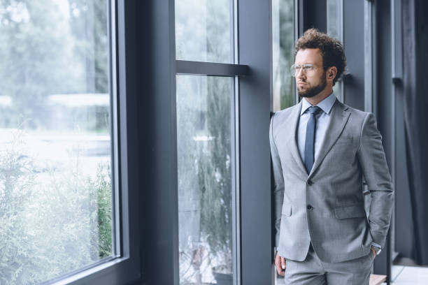 istock young pensive businessman in suit looking out window in office 819674534