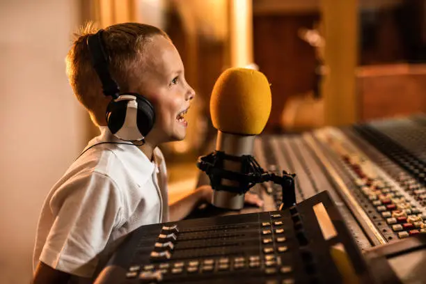 Photo of Happy little boy talking on a microphone in a radio station.