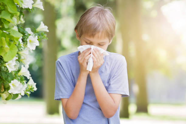 istock Allergy. Little boy is blowing his nose near tree in bloom. 819700296