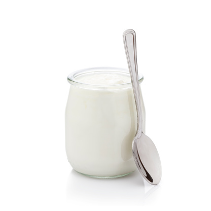 Front view of an open glass container filled with fresh yogurt isolated on white background. A spoon of is beside the container. DSRL studio photo taken with Canon EOS 5D Mk II and Canon EF 100mm f/2.8L Macro IS USM