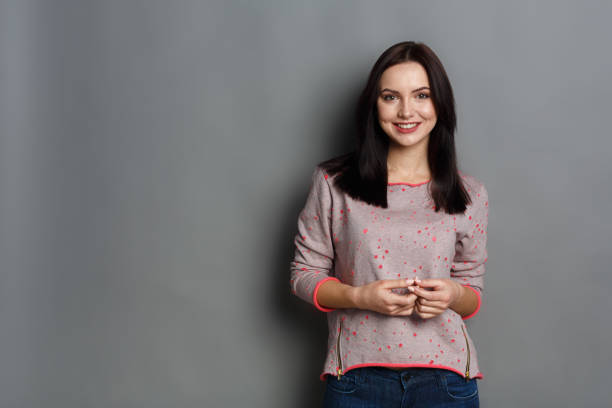 Feeling happy. Cheerful woman expressing joy, wearing casual clothes looking to camera on gray studio background