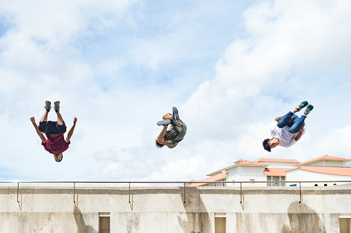 Three adolescent males perform flips off a high ledge