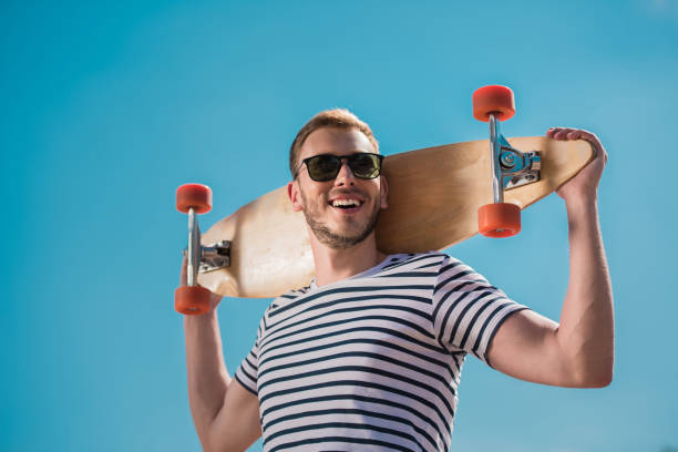 istock happy handsome man in sunglasses holding skateboard, blue sky on background 819766642