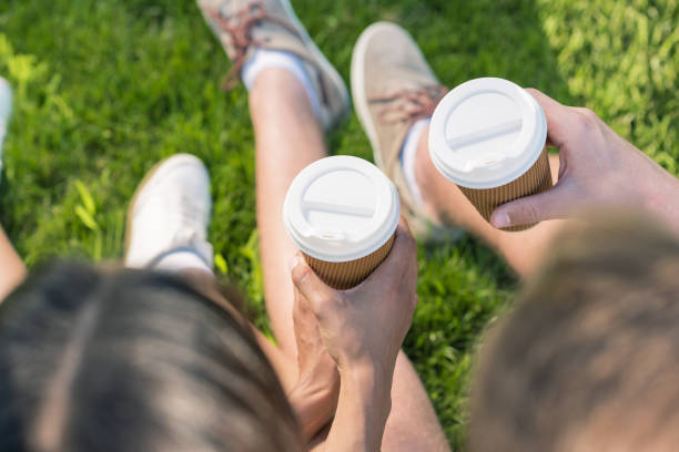 istock couple drinking coffee from paper cups while sitting on grass 819772048