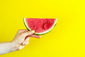 Beautiful feminine hands holding fresh tasty red appetizing watermelon on bright yellow background. Summer Concept.