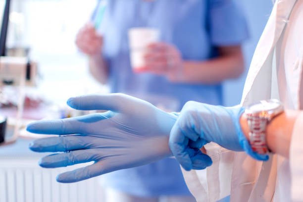 Close up of female doctor's hands putting on blue sterilized surgical gloves in the medical clinic. Close up of female doctor's hands putting on blue sterilized surgical gloves in the medical clinic. dental equipment hand stock pictures, royalty-free photos & images