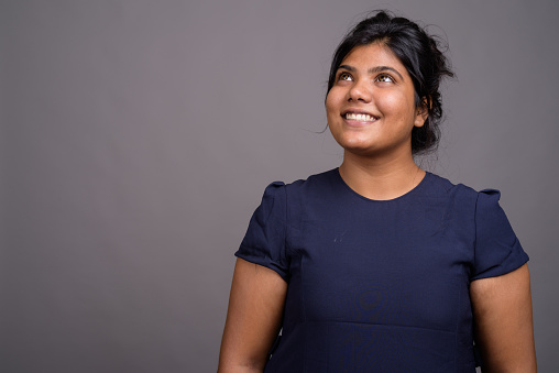 Studio shot of young overweight beautiful Indian woman against gray background horizontal shot