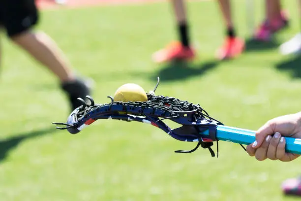 A high school girls lacrosse athlete balances a yellow ball on the back of her stick for fun.