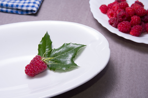 Raspberry on white plate with the leaf on the plate