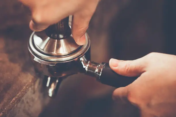 Barista presses ground coffee using tamper. Close-up view on hands with portafilter, small coffee business concept. color vintage style ,Thailand