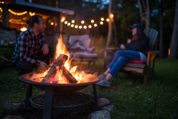 若い家族はキャンプファイヤーの近く美しいカナダ シャレーでは夜遅くに地球温暖化します。 - キャンプファイヤー ストックフォトと画像