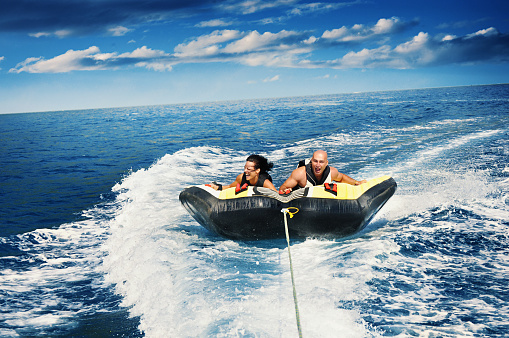 Closeup front view of a young man enjoying tubing session at sea on a sunny summer day. They are on an inflatable raft pulled by a speedboat.