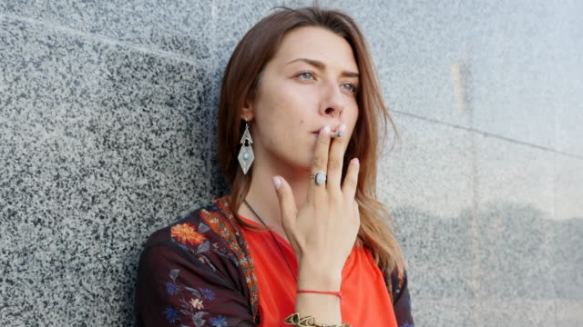 Beautiful young girl smokes a cigarette in the city