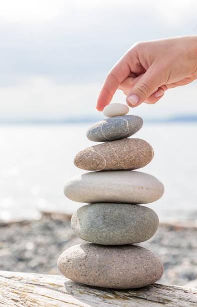 Woman's hand balancing stacking stones on a beach driftwood log with ocean sea in background