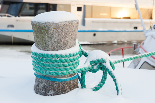 Snow covered bollard with mooring ropes at winter