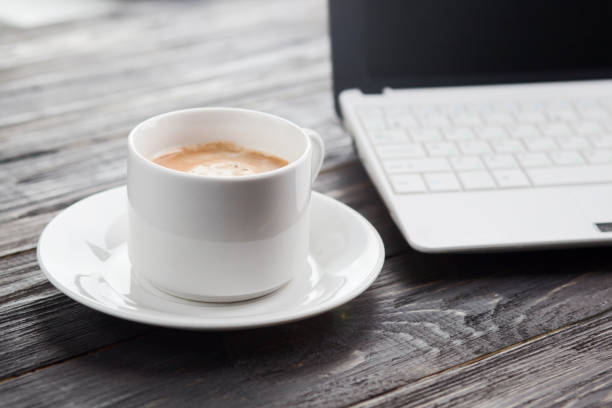 istock Coffee cup close up and laptop as background on rustic wooden table 820073240