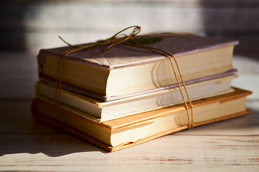 Stack of books, tied with brown twine, on the table near the window with the sun light.