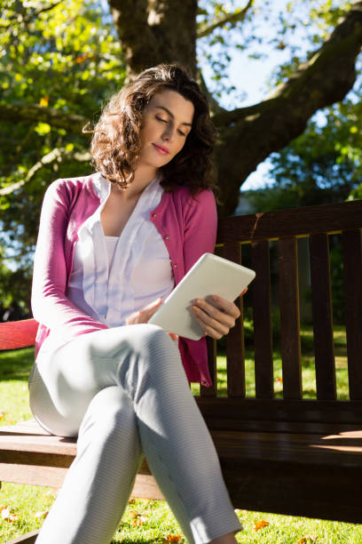 istock Woman sitting on bench and using digital tablet in garden 820105346