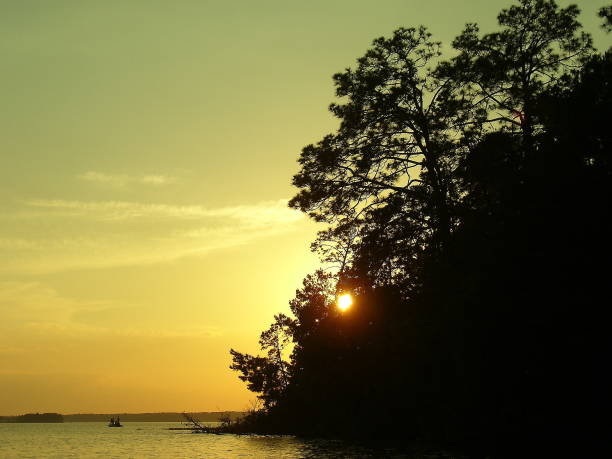 Sunset behind a peninsula in a large lake. Shows a small fishing boat in the water.