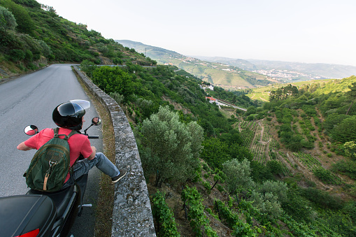 Moto traveller stands and looks from the high road on a green hilly valley.