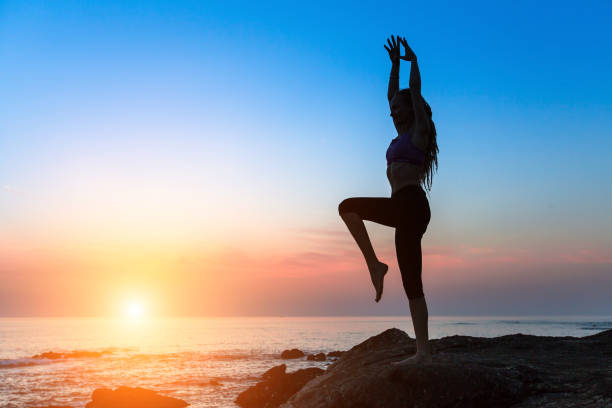 Silhouette of dancing young slim woman on the ocean coast during an amazing sunset. Silhouette of dancing young slim woman on the ocean coast during an amazing sunset. yoga stock pictures, royalty-free photos & images