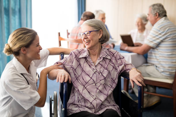 Cheerful disabled senior woman sitting on wheelchair looking at female doctor Cheerful disabled senior woman sitting on wheelchair looking at female doctor in retirement home wavebreakmedia stock pictures, royalty-free photos & images