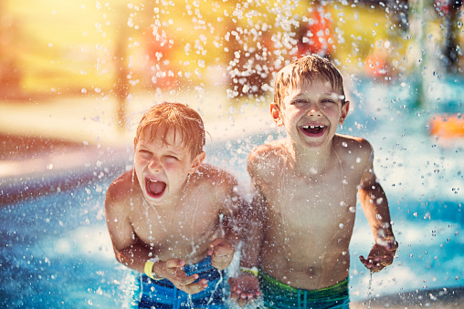 Little boys having fun in splash pool in a waterpark. Laughing and screaming boys are being splashed by water.\n
