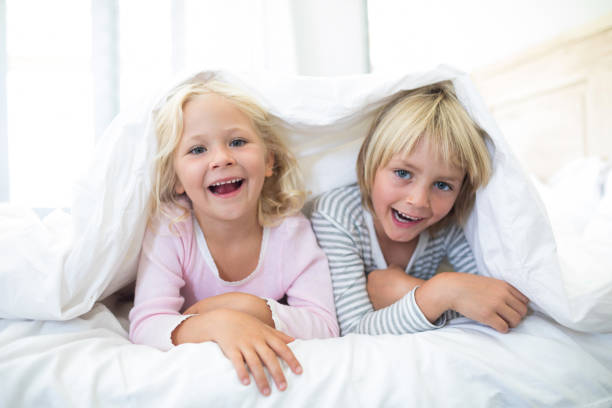 istock Happy siblings lying under blanket on bed in bedroom 820305212