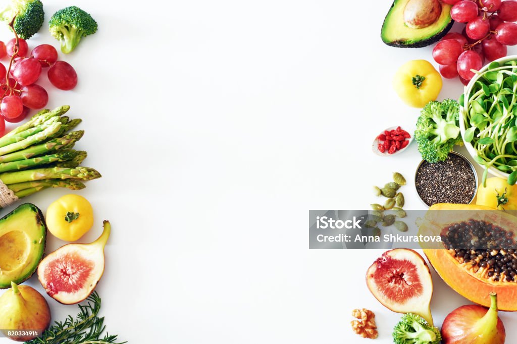 Fresh veggies and fruits food frame on white background with copy space. Detox or clean-eating concept with avocado, papaya, grape, broccoli, figs, nuts, seeds, superfoods. Vegetable Stock Photo