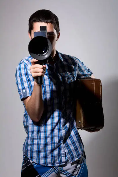 Young man filmmaker with old movie camera and a suitcase in his hand.