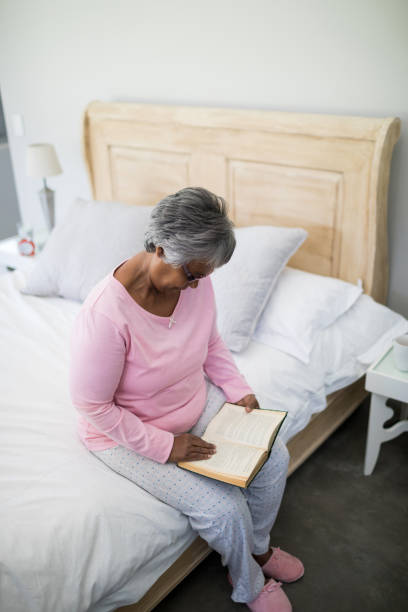 istock Senior woman reading book while sitting on bed in the bed room 820361792