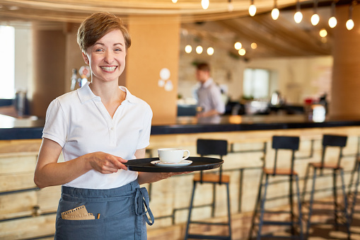 Hospitable waitress holding tray with cup of coffee