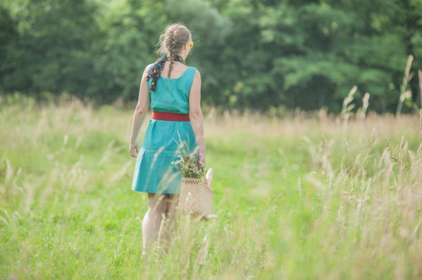 Young Woman Walking in the Summer Meadow, Wearing Corb with Flower and Bread