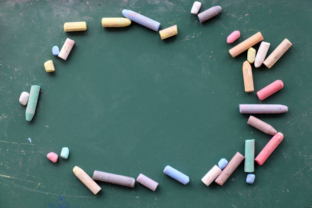 Used chalks of different colors and sizes put as a frame for a text on green chalkboard