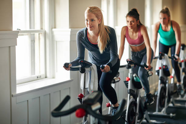 Keep calm and spin on Shot of a young woman working out with an exercise bike in a exercising class at the gym spin bike stock pictures, royalty-free photos & images