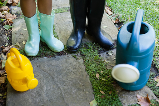 Low section of senior woman and granddaughter standing by watering cans on walkway at backyard
