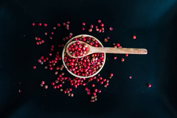 pepe rosa pepe grani in ciotola di legno e cucchiaio su sfondo nero. vista dall'alto. copiare lo spazio. messa a fuoco selettiva. - pink peppercorn foto e immagini stock