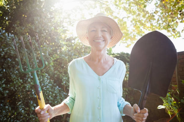 retrato iluminado volta de sorrindo sênior mulher segurando a pá e forquilha do jardim - life back lit people happiness - fotografias e filmes do acervo