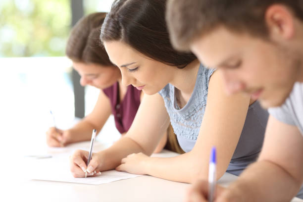 Students doing an exam in a classroom Close up of three concentrated students doing an exam in a classroom writing workshop stock pictures, royalty-free photos & images