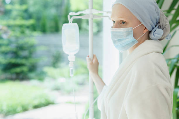 Woman by the window Young woman with drip standing by the hospital window chemotherapy drug stock pictures, royalty-free photos & images