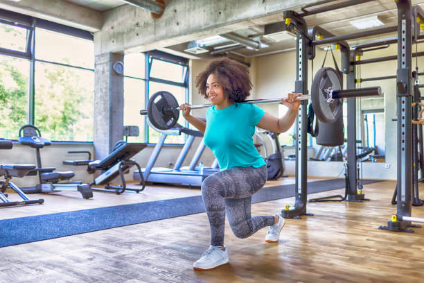 jovem mulher praticando com halteres no ginásio - crouching exercising women barbell - fotografias e filmes do acervo