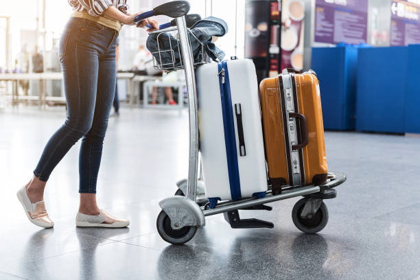 Woman carrying suitcases across hall of airport Female person is walking through airport-foyer with her luggage at small cart. Focus on baggage. Close up of her legs airport check in counter photos stock pictures, royalty-free photos & images