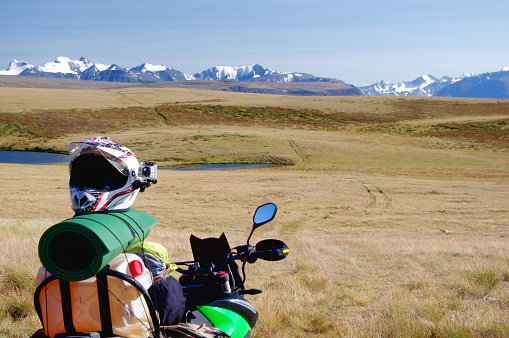Motorcycle enduro traveler alone under a blue sky with white clouds on a background of mountain valley with  snow ice covered mountains peaks and glaciers