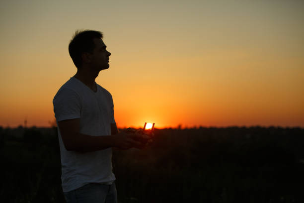 istock Silhouette of a man piloting drone in the air with a remote controller in his hands on sunset. Pilot takes aerial photos and videos with quadcopter from above 820587632