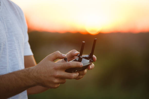 istock Man holds a drone remote controller in his hands. Close-up of quadrocopter RC during flight. Pilot takes aerial photos and videos with quad on sunset 820587762