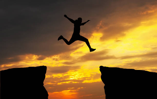 Photo of Man jumping across the gap from one rock to cling to the other. Man jumping over rocks with gap. Element of design.