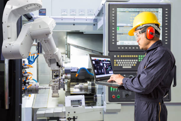 Engineer using laptop computer for maintenance automatic robotic arm with CNC machine in smart factory. Industry 4.0 concept stock photo