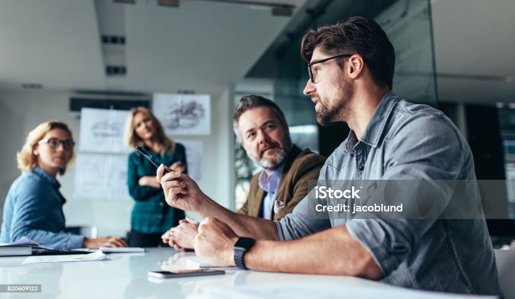 Team of professionals discussing over new business project Young designer giving some new ideas about project to his partners in conference room. Business people discussing over new business project in office. Meeting Stock Photo